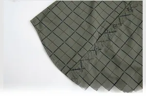 Detailed close-up of the curved shirt hem showing green plaid fabric and neat stitching