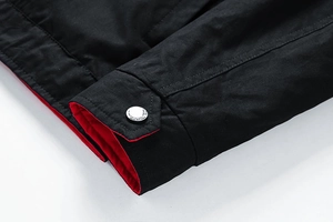 Detail of silver metal snap button on a black reversible jacket sleeve with red lining