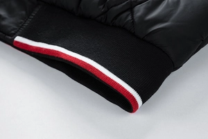 Detailed macro view of black quilted jacket featuring red and white striped ribbed cuffs