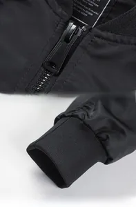 Detail of metal zipper and elastic ribbed cuff on a black bomber jacket with micro-sheen