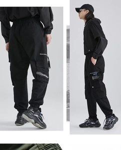 Detail view of black techwear cargo pants featuring multi-pocket design and printed straps