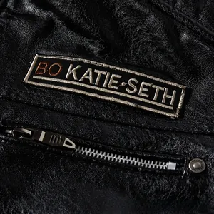 Detail of black faux leather biker jacket with BO KATIE SETH embroidery and metal zippers