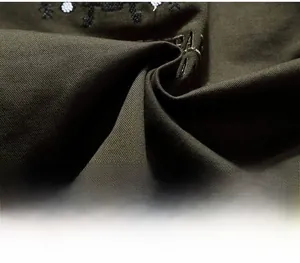 Detailed close-up of olive green military jacket fabric with black embroidery and twill texture