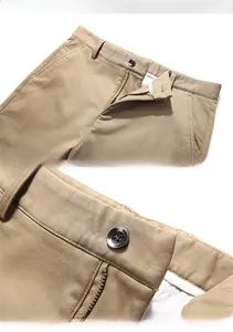 Detail view of khaki cotton trousers showing waist stitching, button and zipper closure