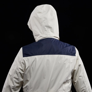 Rear view of outdoor hooded jacket showing dark blue shoulder panels and cream fabric