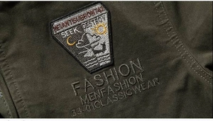 Detail of dark olive tactical jacket with embroidered shield patch and canvas texture
