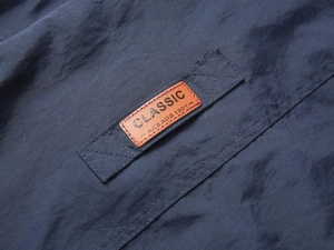 Dettaglio dell'etichetta in pelle marrone classica con cuciture a croce su gilet blu scuro