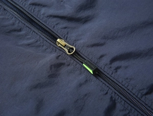 Dettaglio del gilet da esterno blu scuro con cerniera in metallo e tiretto verde neon