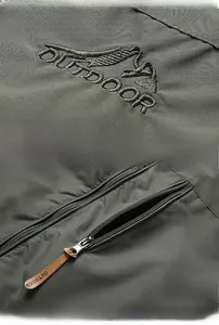 Détail macro du logo de montagne brodé et poche zippée sur la veste outdoor vert olive