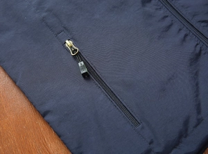 Dettaglio di un gilet outdoor blu scuro con tasca con zip e linguetta in metallo
