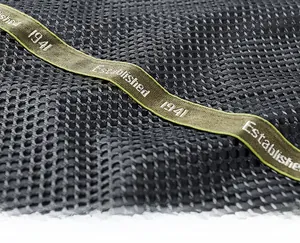 Macro shot of olive green webbing on black honeycomb mesh fabric with silver lettering