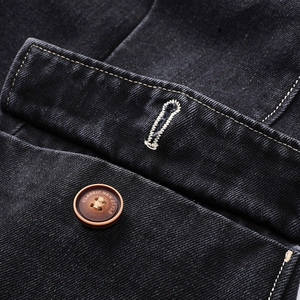 Detailed close-up of premium black denim jacket pocket with classic engraved button