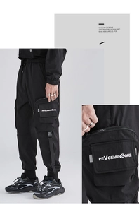 Dettaglio di joggers cargo techwear neri con tasche a zip e stampa logo da uomo
