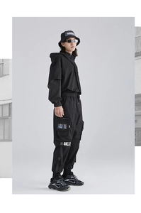 Dettaglio dei pantaloni cargo techwear neri con stampa GREAT bianca e finestra tasca trasparente