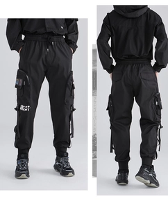 Dettaglio dei pantaloni cargo techwear neri con tasche multiple, badge stampati e coulisse