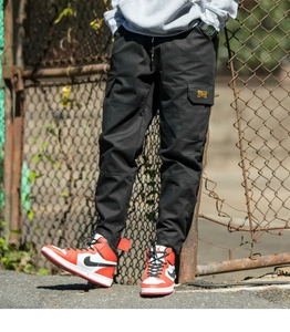 Detail view of black cargo pants featuring large side flap pockets and cuffed leg openings