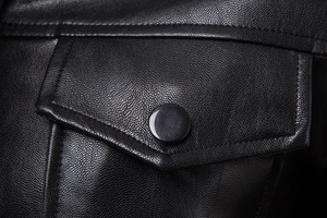 Detailed macro view of a black leather hooded jacket featuring a snap flap pocket