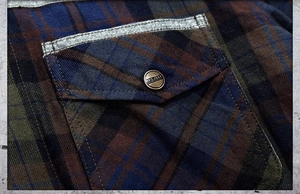 Macro detail of men's plaid flannel shirt featuring a pocket with metal button and piping