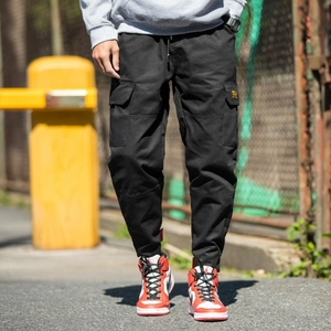 Men's black cargo joggers with side pockets and yellow label in urban street setting