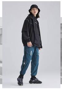 Detail of dark blue technical cargo pants featuring multiple pockets and reflective piping