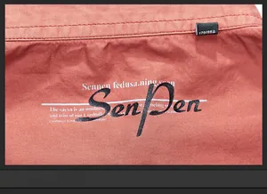Close-up of brick red cotton shirt texture with SenPen print and size label detail