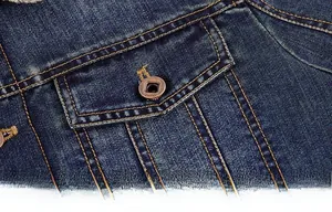 Detail of dark blue denim jacket chest pocket with yellow stitching and metal button