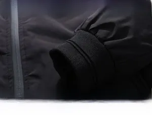 Dettaglio di un piumino nero antivento con tasca a zip e polsini elasticizzati