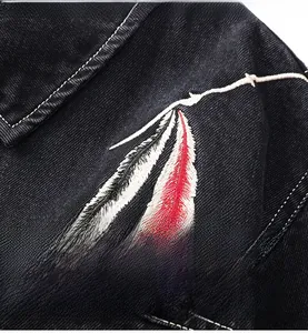 Detailed close-up of feather embroidery on black denim twill jacket fabric texture