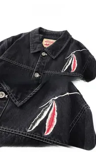 Detail of black denim jacket featuring intricate feather embroidery and metal buttons