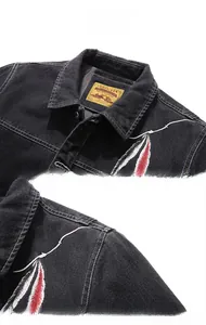 Détail du col d'une veste en jean noire avec broderie de plumes colorées