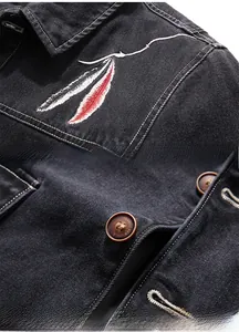 Détails de broderie plume rouge et blanche et boutons métalliques sur veste en jean noire