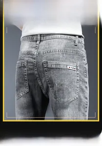 Close-up of men's gray slim-fit denim jeans featuring a woven Y-B label on the back pocket