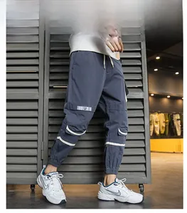 Dettaglio dei pantaloni cargo blu-grigio con grandi tasche e finiture riflettenti a nastro U