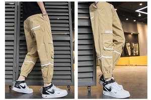 Dettaglio dei jogger cargo kaki con grandi tasche e accenti a strisce bianche