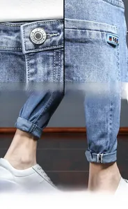 Detail view of light blue denim fabric with metal button and tapered leg cuffs for men