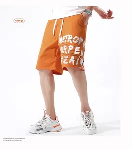 Détail du short cargo orange avec lettrage graffiti blanc et taille élastique à cordon