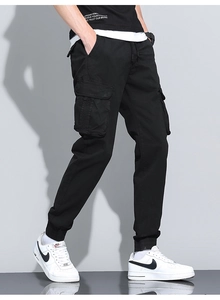 Detail of black cotton cargo jogger pants with functional side flap pockets and ribbed cuffs
