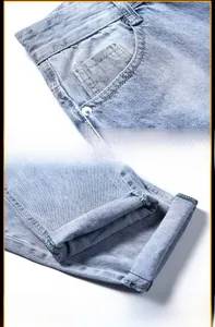 Détail du jean délavé bleu clair avec coutures contrastées vertes sur les revers du pantalon