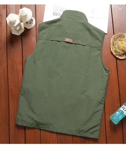 Back view of army green outdoor vest with leather tag on dark wooden background