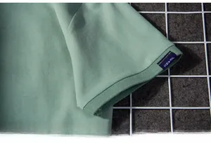 Close-up of piqué polo shirt cuff in sage green with ribbing and blue woven JEANS label