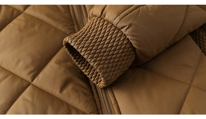 Détail macro de la veste matelassée caramel montrant les poignets tissés et coutures de qualité