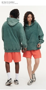 Detail of acid-washed green heavy cotton hoodie and bright orange shorts on models