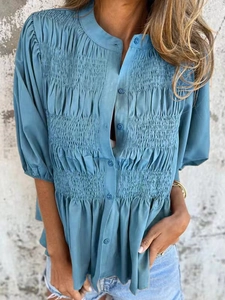 Detail of grey-blue blouse showing smocked bodice texture and round neck buttons