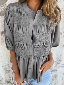 Detail of grey short sleeve shirt showing smocked pleats and buttoned round neckline