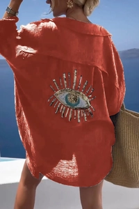 Detail of sequined evil eye embroidery on the back of a brick red crinkle fabric shirt