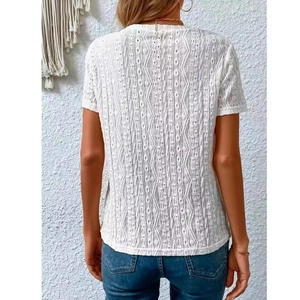 Detail of white short sleeve top featuring geometric hollow embroidery and textured fabric