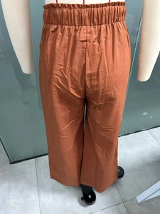 Dettaglio dei pantaloni a gamba larga in lino con vita alta e texture color terracotta