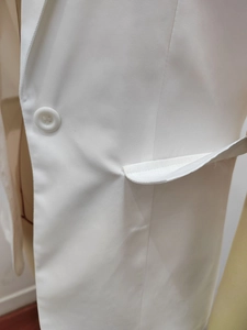 Close-up of white summer blazer featuring single-breasted button and flap pocket detail