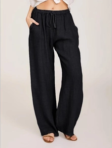 Detail of loose black linen pants showing elastic waist with drawstring and natural fabric