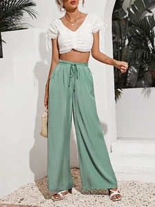 Dettaglio dei pantaloni a gamba larga in raso verde salvia a vita alta con coulisse